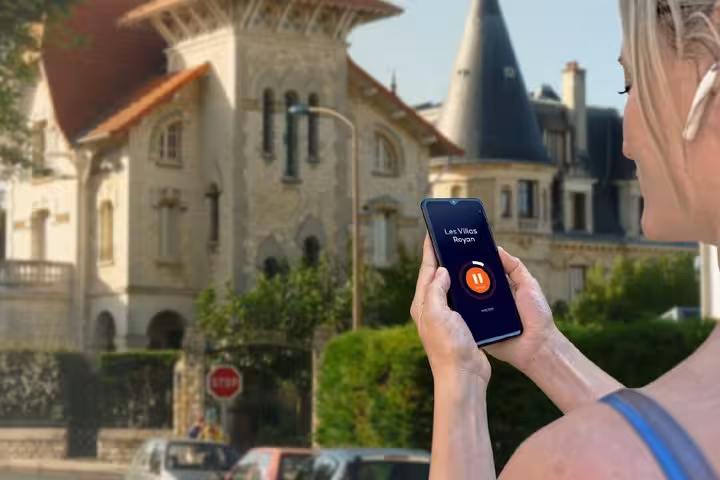 Woman using audio guide app on smartphone for self-guided walking tour of historic villas in Royan, France