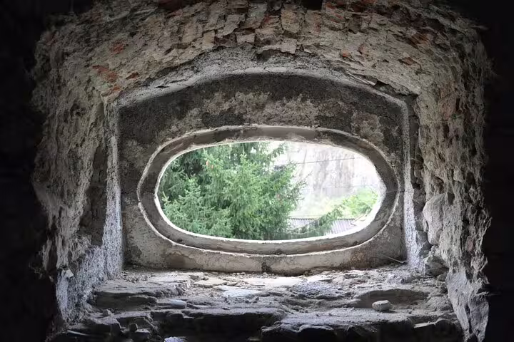 Ancient oval stone window inside Rupea Fortress walls with green trees visible outside
