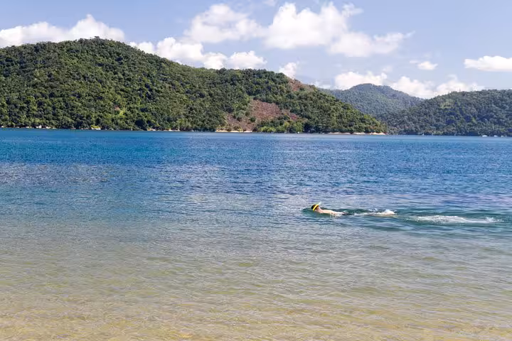 A swimmer enjoying the tranquil waters of Saco Mamanguá Fjord, surrounded by stunning green hills and blue skies.