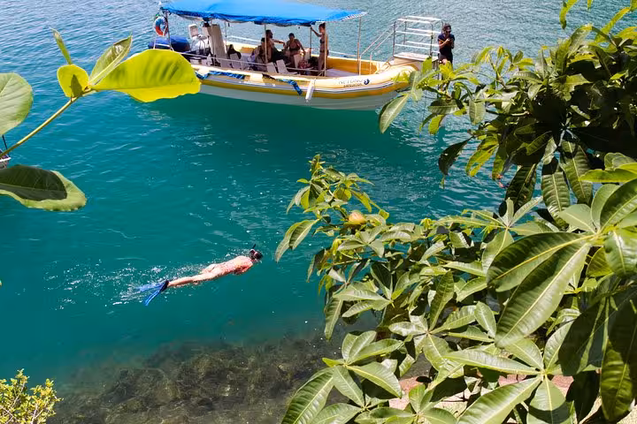 Tourists enjoying a boat ride while a snorkeler explores vibrant waters at Saco Mamanguá Fjord during half-day tour.
