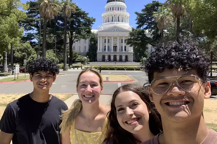 Four smiling friends taking a selfie in front of the California State Capitol building in Sacramento