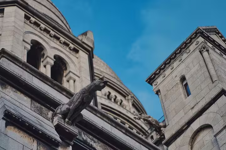 Gargoyle statues on the exterior of Sacré-Cœur Basilica in Montmartre, Paris, with dome and blue sky