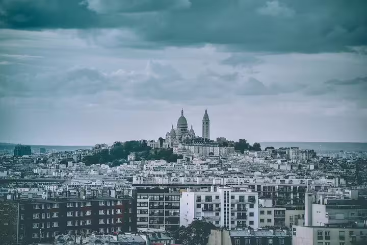 Panoramic view of Paris with Sacré-Cœur Basilica atop Montmartre hill under dramatic cloudy sky