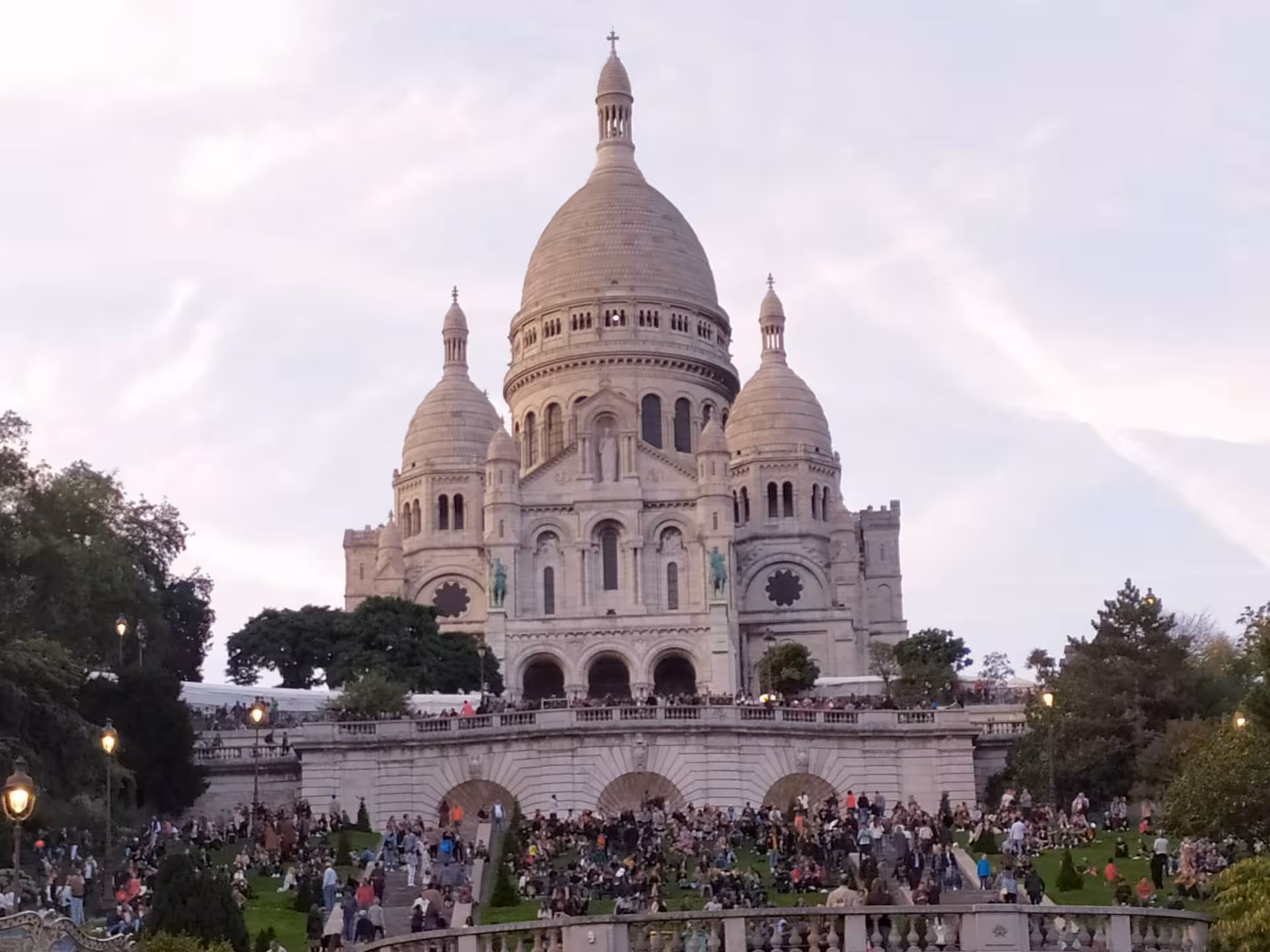 Crowds gathered on the steps and lawns below Sacré-Cœur Basilica at dusk in Montmartre, Paris