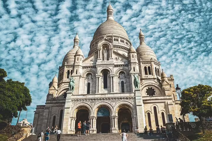 Sacré-Cœur Basilica facade with tourists on steps in Montmartre, Paris under a dramatic cloudy sky