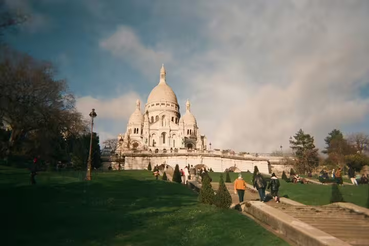 Sacré-Cœur Basilica on Montmartre hill with green lawns and tourists on a sunny day in Paris