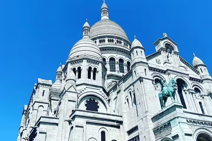 Sacré-Cœur Basilica white stone domes and facade against blue sky in Montmartre, Paris