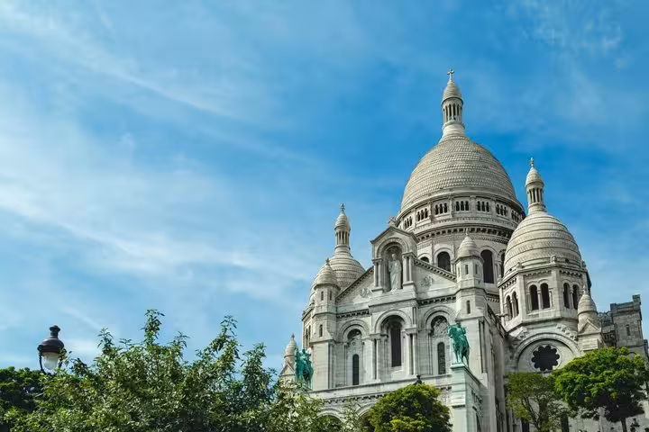 Sacré-Cœur Basilica white domed exterior with green trees under blue sky, Paris