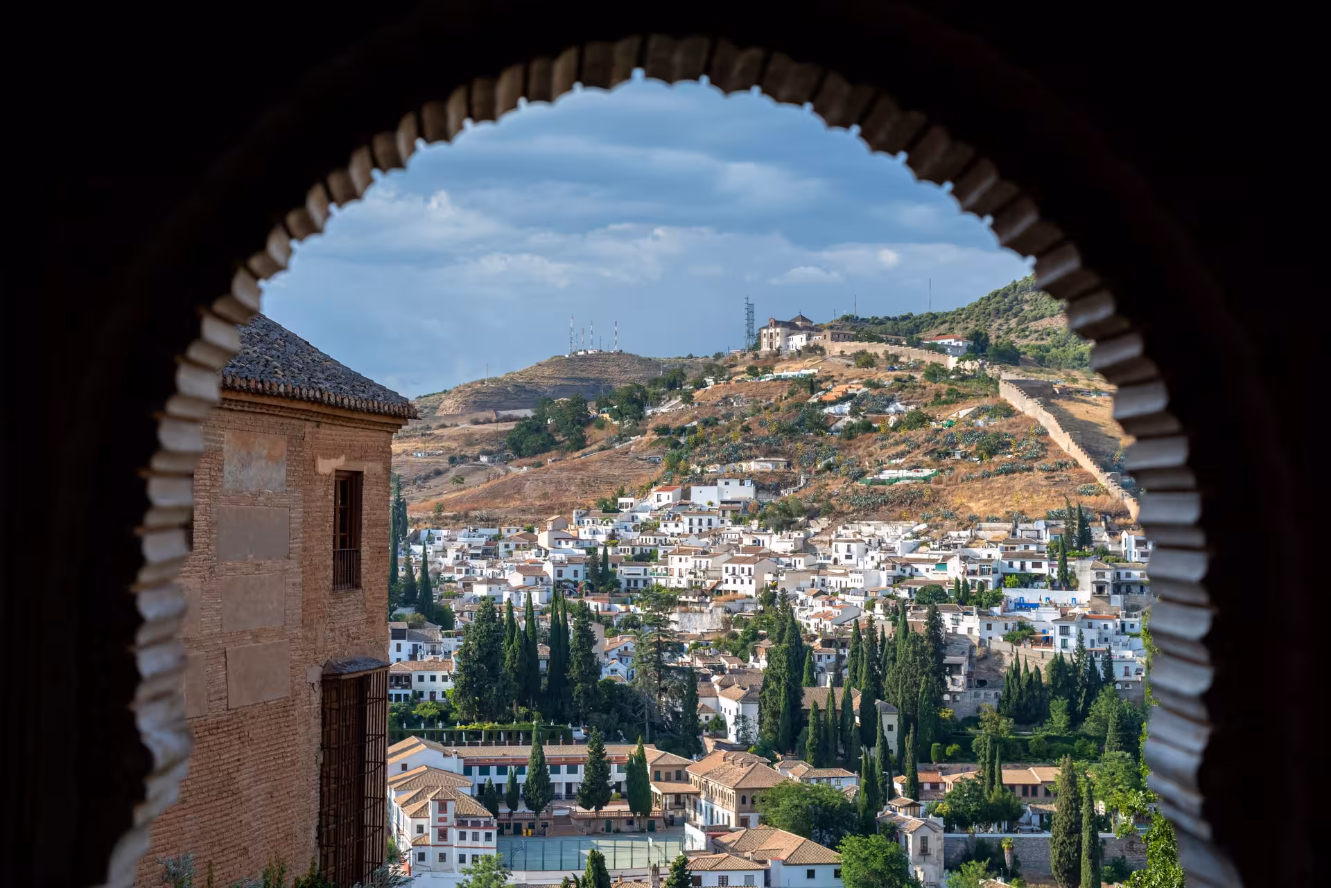 Scenic view through an archway of Sacromonte's hillside homes, surrounded by lush greenery and rolling hills.