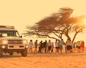 Group of tourists walking near Toyota jeep by desert tree at sunset in Safaga desert safari