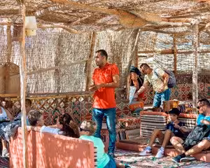 Guide speaking to tourists under a traditional Bedouin tent shelter during a desert safari excursion in Safaga