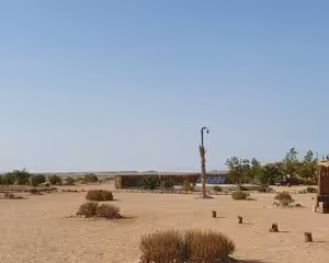 Sandy desert landscape with sparse vegetation and a lone lamppost near a building in Safaga, Egypt