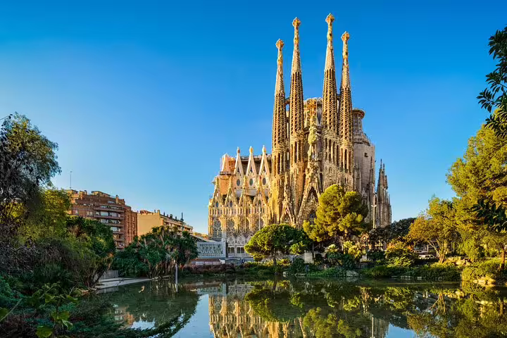 Stunning view of the Sagrada Familia in Barcelona reflecting in a serene pond under a clear blue sky.