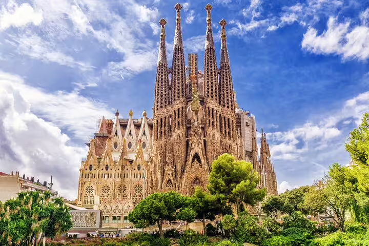 Sagrada Familia cathedral towers with ornate Gothic facade surrounded by green trees in Barcelona
