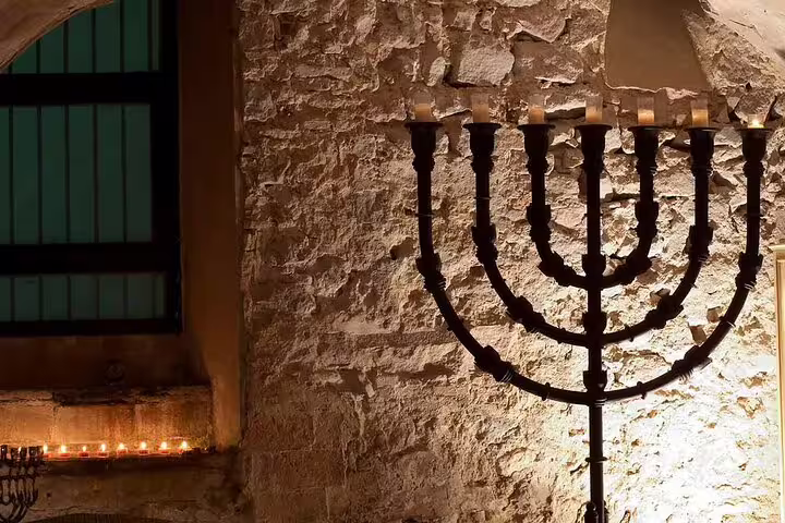 Dimly lit ancient stone wall with a large, traditional menorah, highlighting the Jewish heritage in the tour of Sagrada Familia, Romans, and Jewish Quarter.