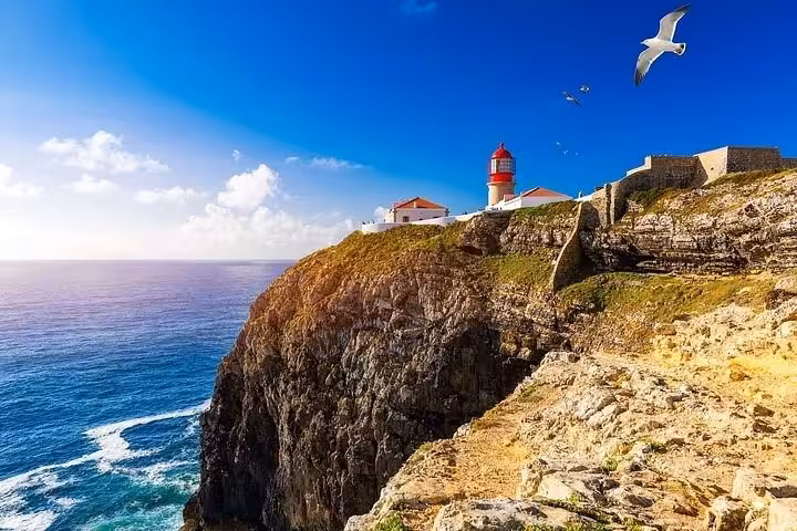 Dramatic Sagres cliffside with red lighthouse, Atlantic Ocean views and seagulls on a sunny Half-Day Tour from Lagos