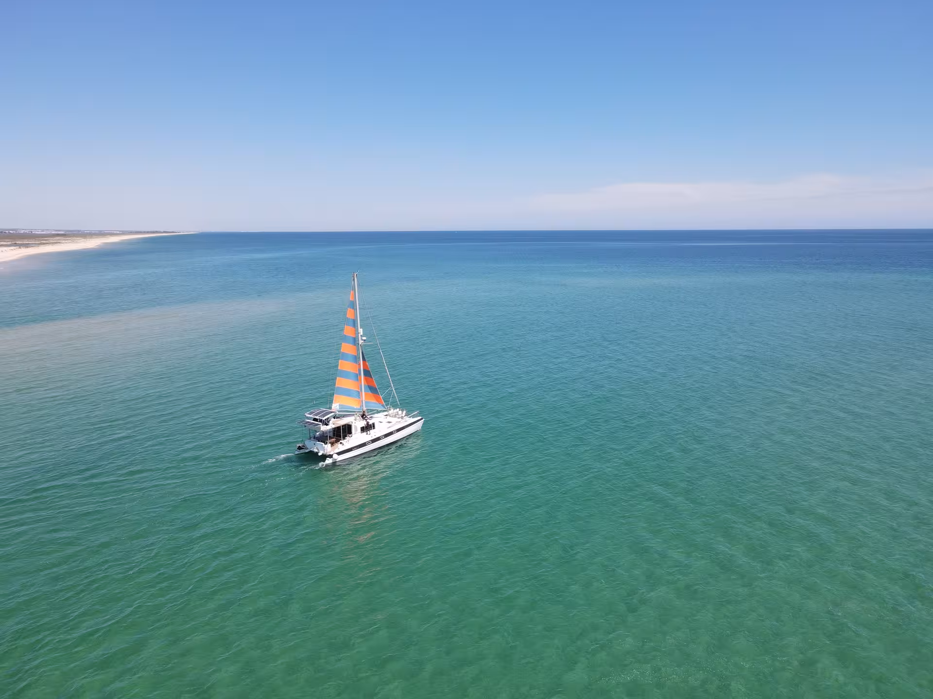 Sail catamaran cruising across calm Atlantic toward the Blue Lagoon on a full-day sailing tour from Faro
