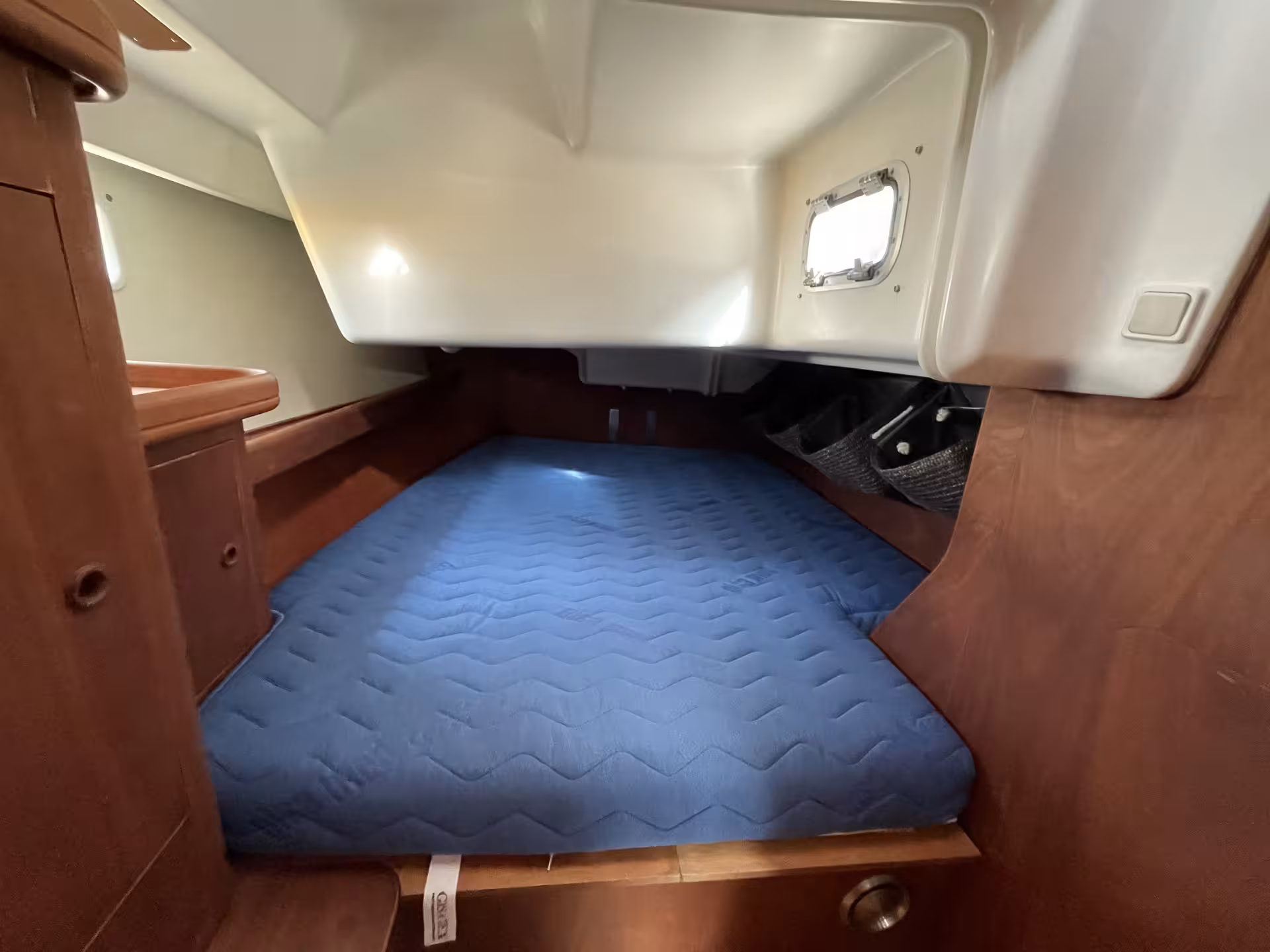 Cozy V-berth cabin with blue mattress and small porthole window on a sailboat French Riviera charter