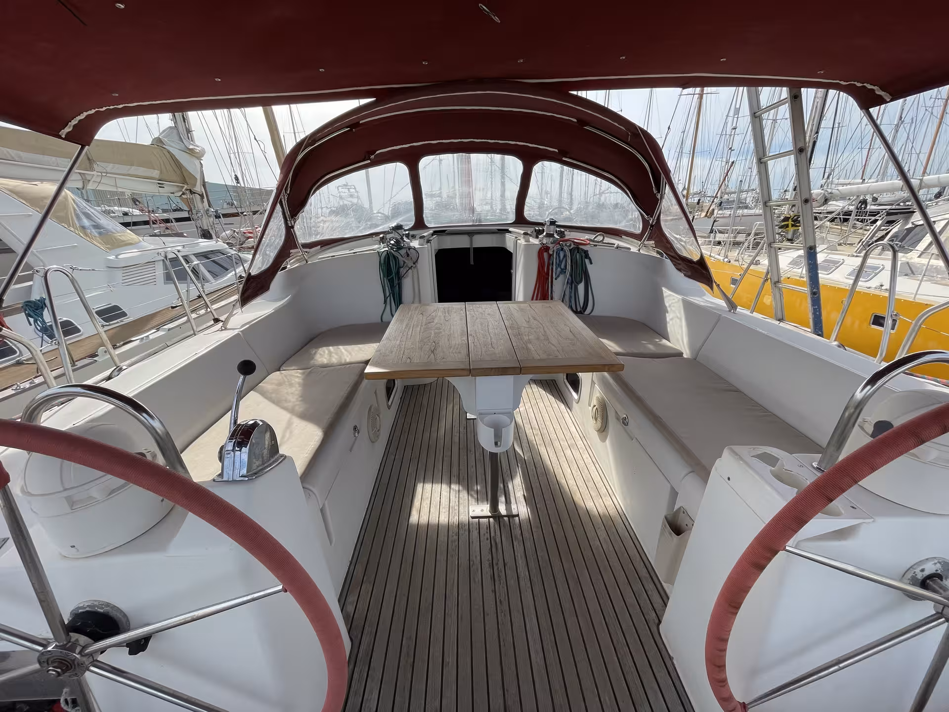 Sailboat cockpit with teak deck, dual red helm wheels, and folding table at French Riviera marina