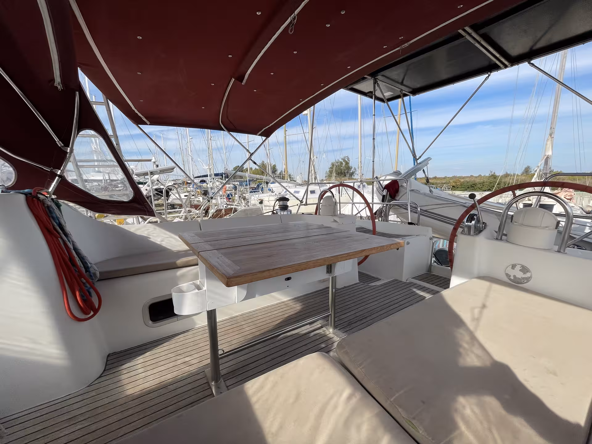 Sailboat cockpit with teak table, dual helm wheels, and marina views on the French Riviera