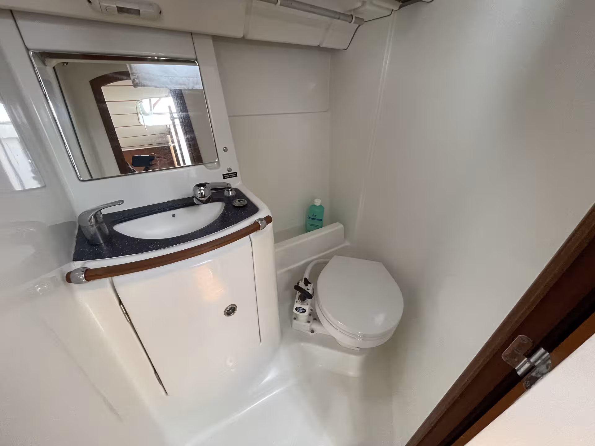 Compact marine bathroom with sink, mirror, and manual toilet on a sailboat