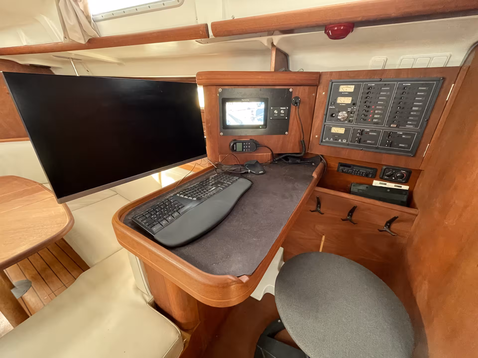 Navigation station with chart plotter, VHF radio, electrical panel, and large monitor inside a sailboat cabin