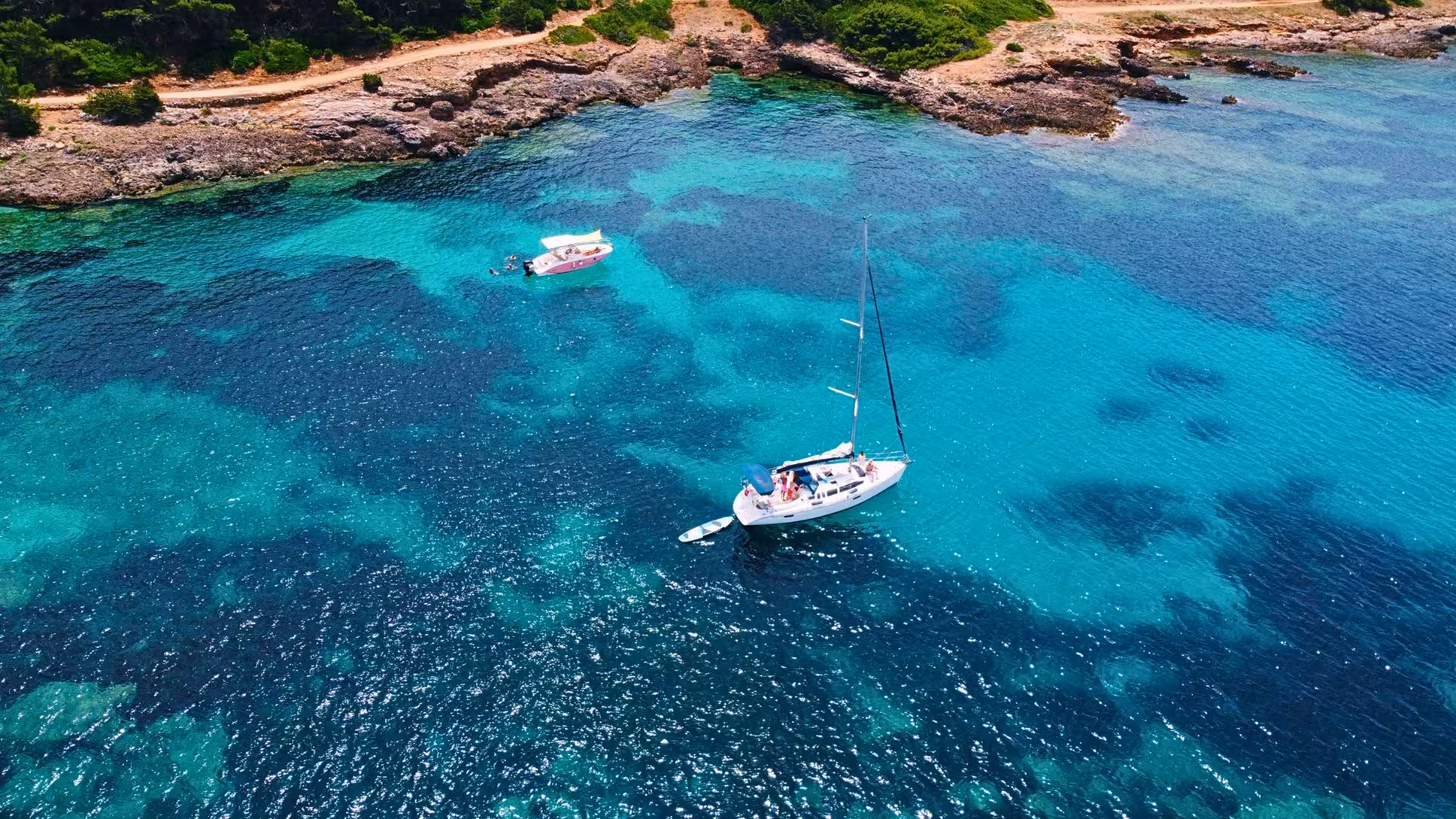Aerial view of a sailboat on turquoise waters in Porto Conte Park, Alghero, showcasing a serene sailing experience.
