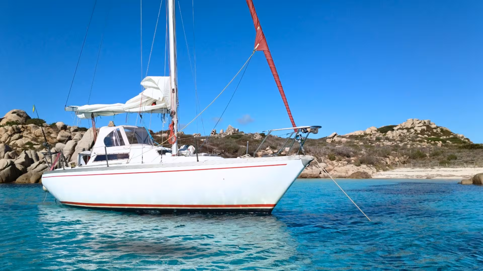 Sailboat anchored in pristine waters near rocky shores, part of a scenic sailing tour from Santa Teresa di Gallura to Corsica.