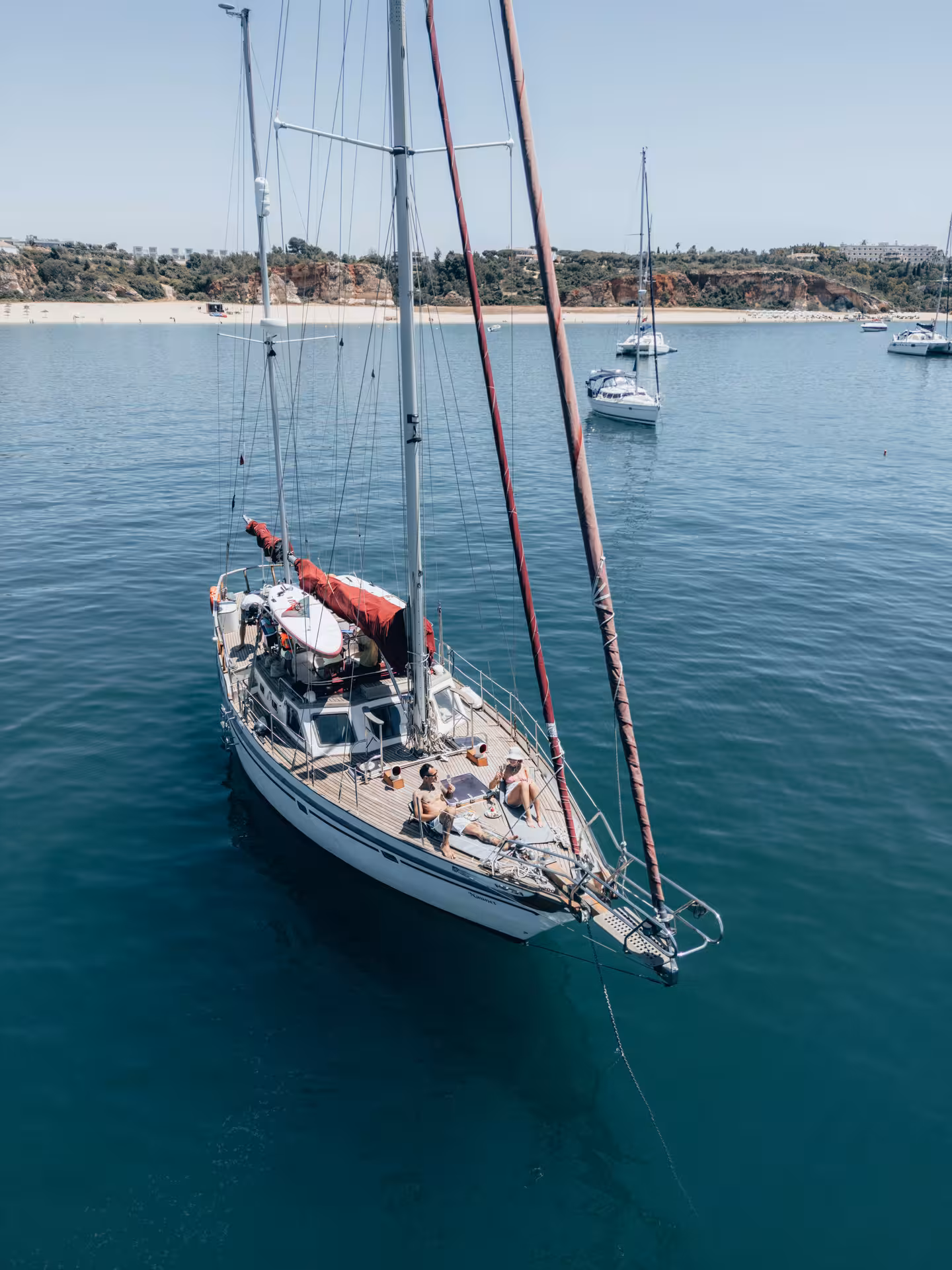 Aerial view of a luxury sailboat anchored near Portimao beach with couple relaxing on deck in Algarve