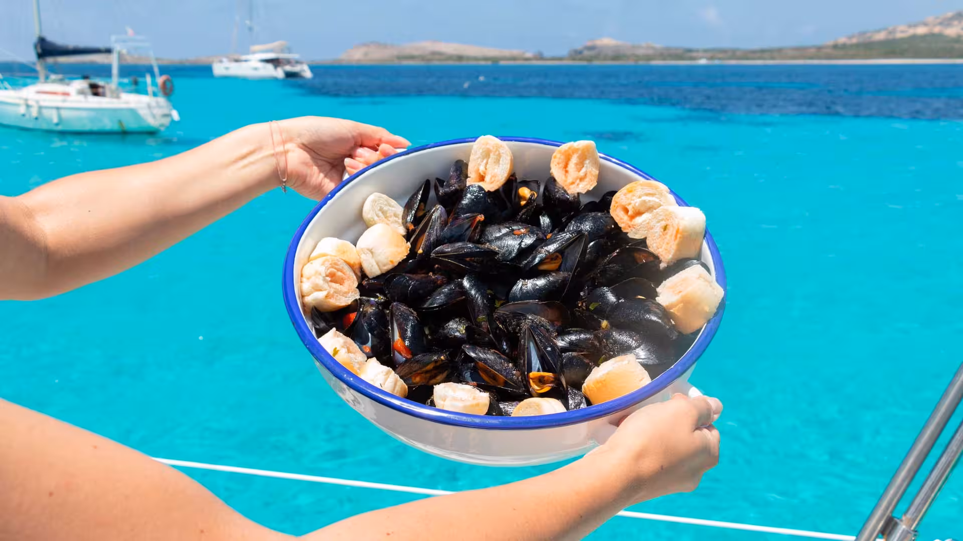 Fresh mussels and bread rolls served on a sailboat with stunning turquoise waters near Asinara.