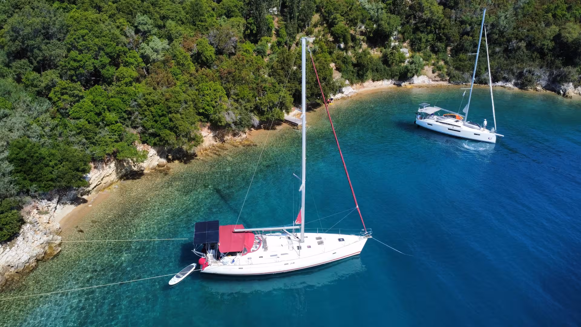 Two white sailboats anchored in a turquoise cove with lush green cliffs on the French Riviera