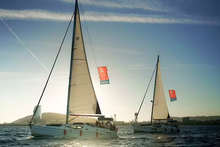 Two sailboats cruising off Barcelona at sunset, offering a scenic Mediterranean sailing experience with skyline views