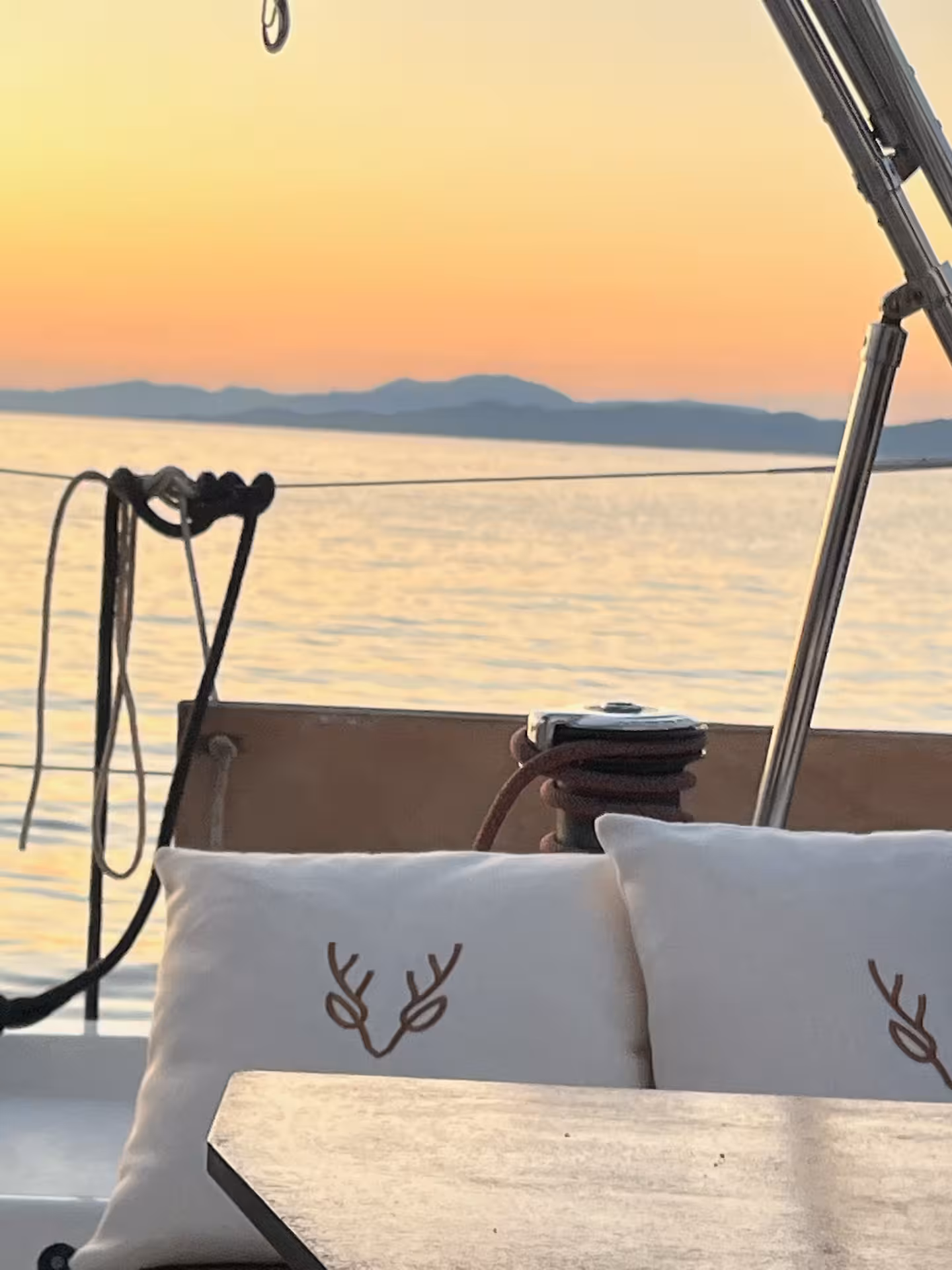 Sailboat cockpit with white cushions at golden sunset over calm Ligurian Sea and coastal mountains