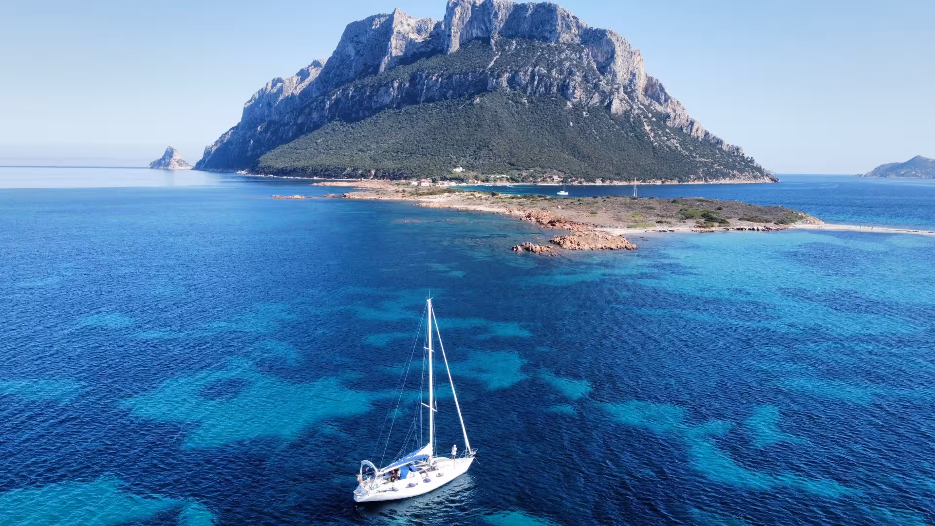 Sailing boat on clear blue waters near a rocky island in San Teodoro, offering breathtaking views and adventure.