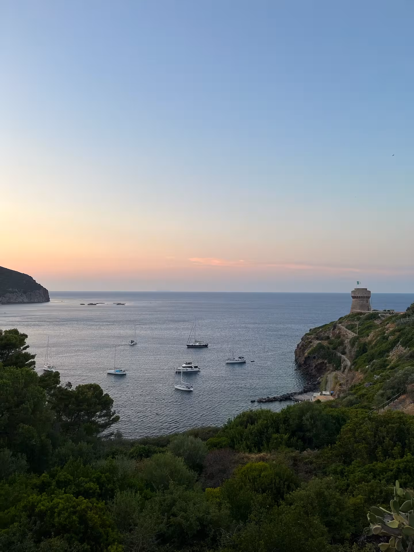Sailboats anchored in a calm bay at sunset near a coastal tower on the Ligurian Coast