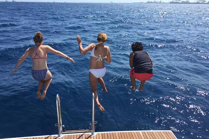 People joyfully jumping off a sailboat into the ocean during an exclusive 3-hour sailing trip with tapas and drinks.