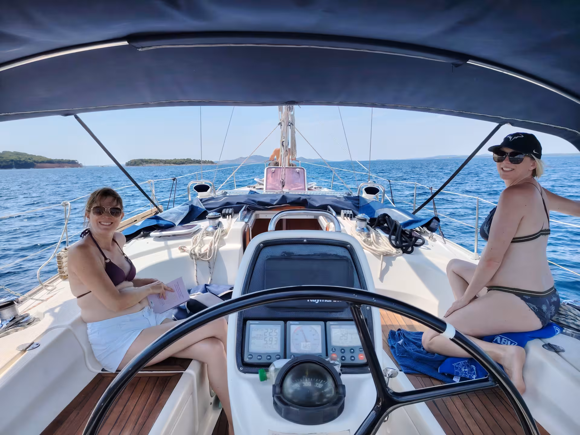 Guests relax in cockpit of sailing yacht on a sunny island-hopping cruise, blue sea and coastline views