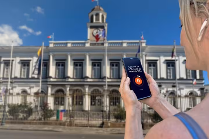 Tourist holding smartphone with audio guide app in front of Saint-Denis Hotel de Ville, Reunion Island