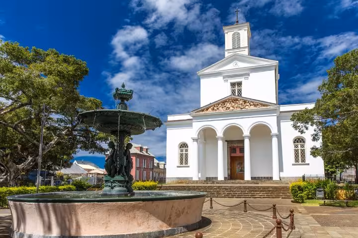 White neoclassical church with arched entrance and green fountain in Saint-Denis, Réunion
