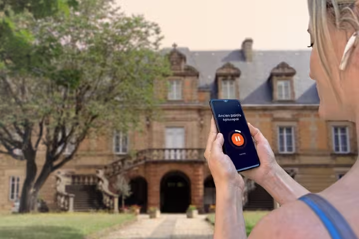 Woman holding smartphone with audio guide app in front of historic Ancien Palais Épiscopal in Saint-Etienne