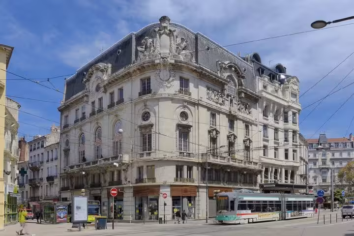 Ornate Beaux-Arts building on a street corner in Saint-Etienne with a tram passing by