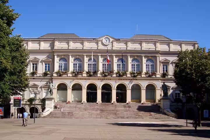 Neoclassical Saint-Etienne City Hall facade with French flags and clock tower on sunny day