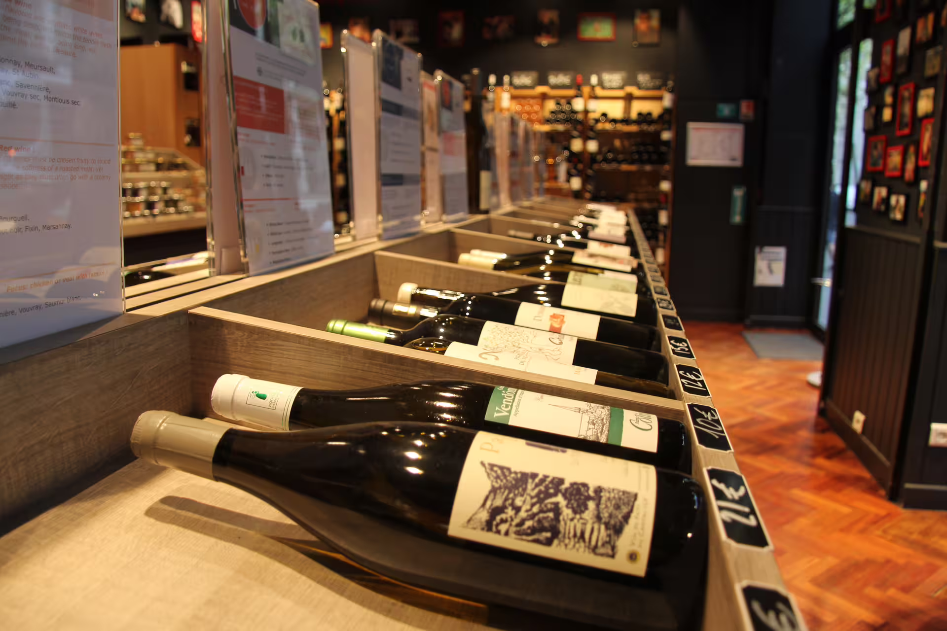 Wine bottles displayed on angled wooden racks in a Parisian wine shop with price tags