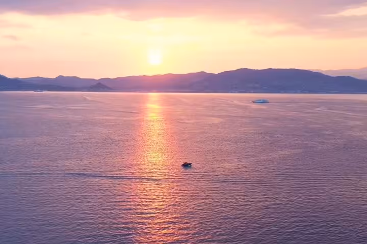 Scenic sunset over calm sea with small boat and mountain silhouette near Saint-Honorat Island