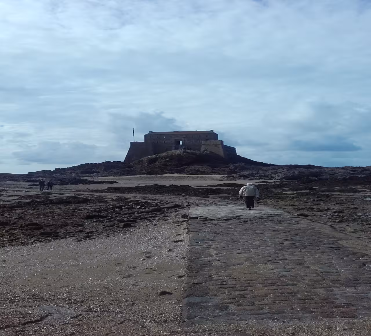 Stone causeway leading to Saint Malo fort on rocky coastline with visitors walking toward entrance