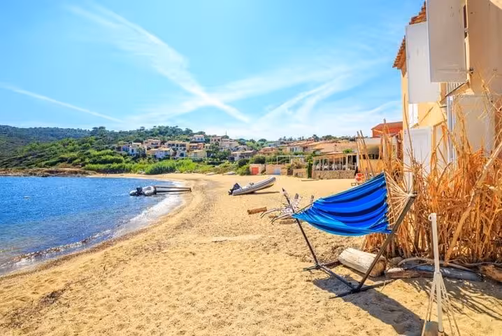Sandy beach with blue hammock, moored boats, and hillside village near Saint Tropez on a sunny day