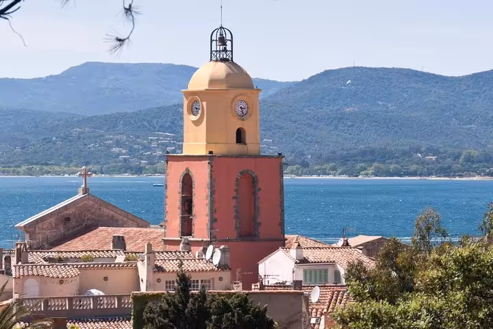 Saint-Tropez church bell tower with yellow dome and clocks overlooking the blue Mediterranean bay