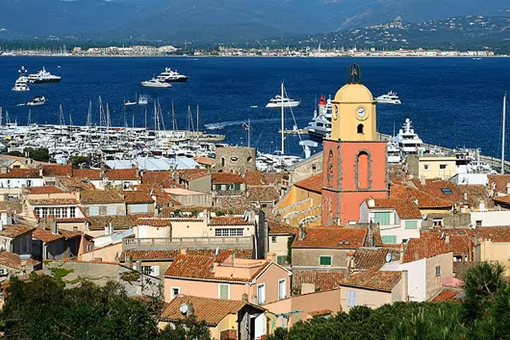 Aerial view of Saint-Tropez old town with clock tower, terracotta rooftops, and luxury yachts in harbor