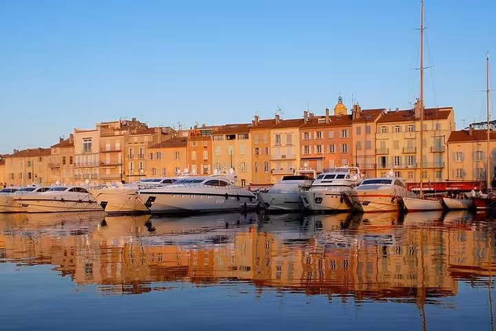 Luxury yachts moored at Saint-Tropez harbor with colorful waterfront buildings reflected in calm water