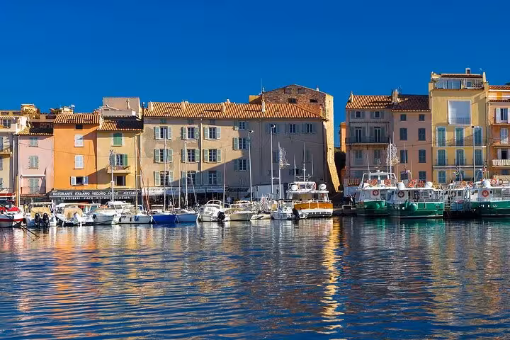 Colorful waterfront buildings and sailboats reflected in the calm harbor of Saint-Tropez on a sunny day